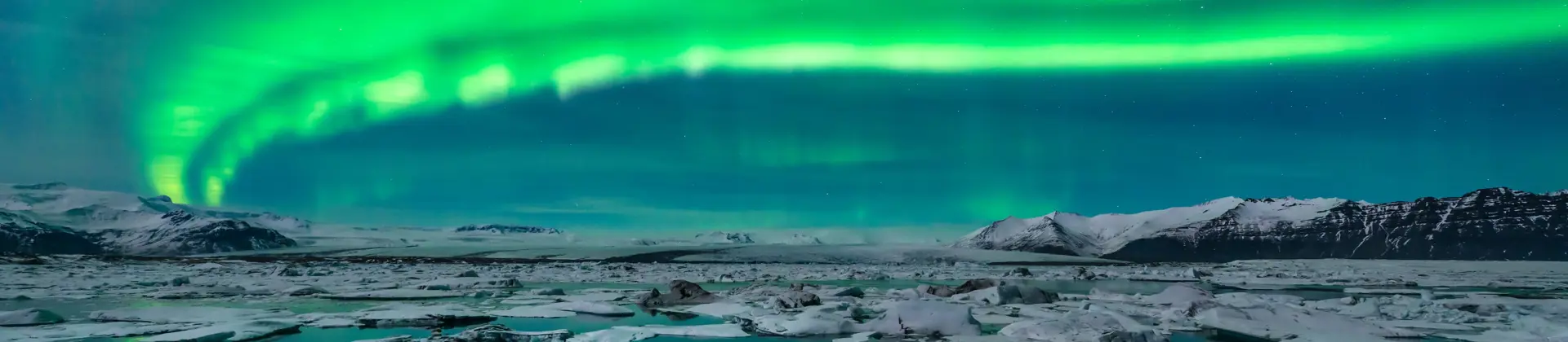 Green northern lights curving from the right back to the left. Below, a lake with ice blocks