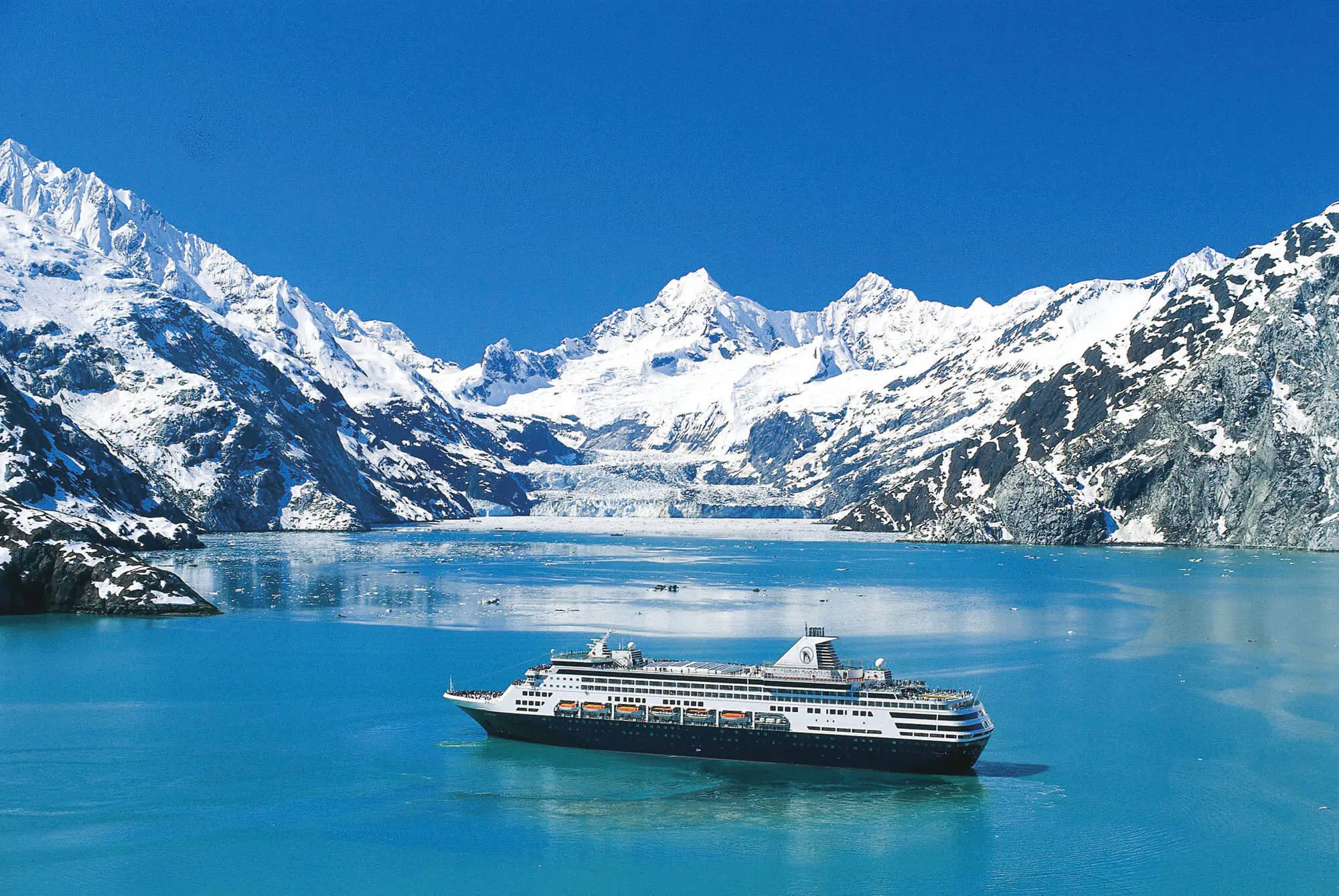 The MS Koningsdam cruise ship sailing through Glacier Bay, surrounded by calm icy waters and dramatic snow-capped mountains
