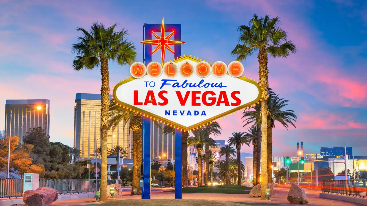 "Welcome to Fabulous Las Vegas, Nevada” sign at dusk, with palm trees and city lights in the background